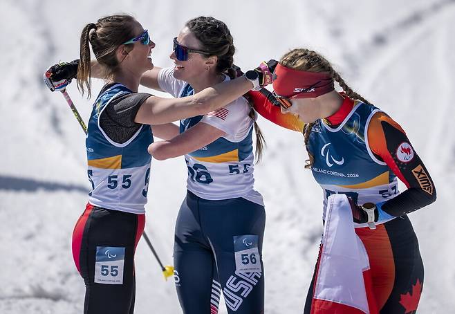 파라 바이애슬론에 출전한 캐나다와 미국의 선수들이 결승선에서 힘든 레이스를 마친 뒤 서로의 어깨를 감싸 쥐고 있다.