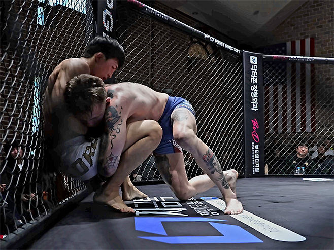 미국팀 레이크 지가 2026년 3월 경기도 오산시 종합격투기 국가대항전 ‘블랙컵’ 준준결승 밴텀급 경기에서 대한민국 알파 ‘리바이’ 김유찬을 넘어뜨리고 있다. 블랙컵 첫 시즌은 유튜브 채널 ‘블랙컴뱃’ 유료 멤버십 단독 생중계다. 사진=이데아 파라곤