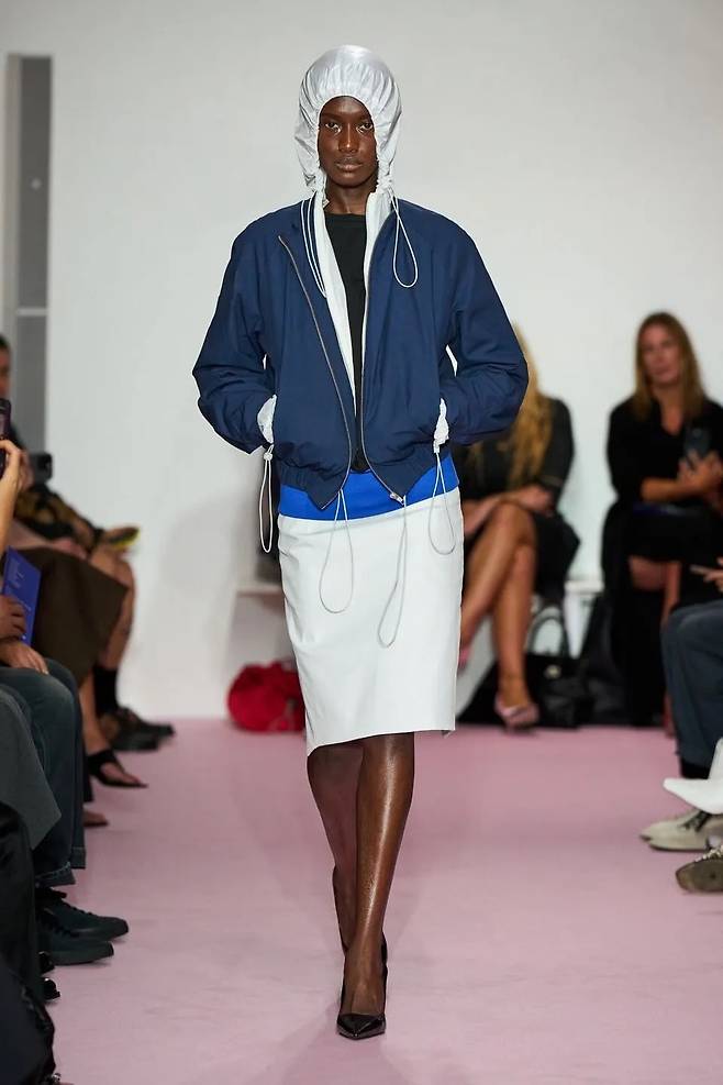 미디 스커트, 펌프스와 함께 세련되게 스타일링 된 스포티 재킷. 리 스튜디오(Lii Studio).