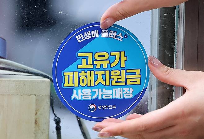 고유가 피해지원금 지급이 시작된 지난달 27일 서울의 한 시장에서 상인이 '고유가 피해지원금 사용가능매장' 스티커를 붙이고 있다. /사진=뉴스1