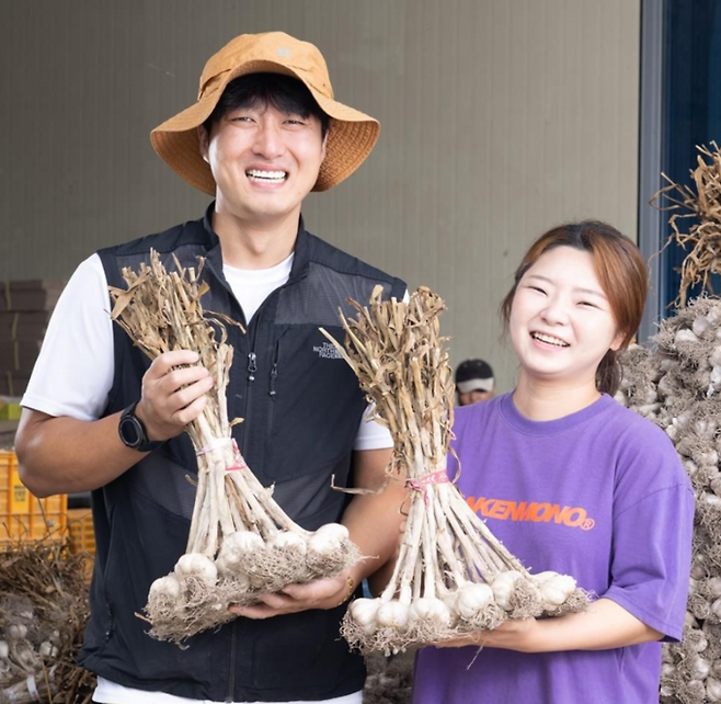 ▲ 행정안전부 '2026년 모두애(愛) 마을기업'에 선정된 의성군 마을기업 ㈜한톨 고희주(오른쪽) 대표 부부가 의성 한지형마늘을 들어 보이며 기념촬영을 하고 있다. ㈜한톨은 지역 농가 35곳과 연계한 마늘 가공·유통 사업으로 최근 3년 평균 매출 12억 원을 기록했다. 의성군 제공