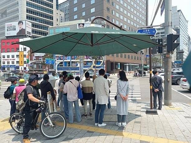 횡단보도를 건너려는 시민들이 그늘막 아래 모여 신호를 기다리고 있다. 사진=스레드 갈무리