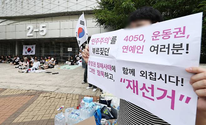 6·3 지방선거 투표지 부족 사태를 규탄하며 재선거를 요구하는 '잠실 개표소 봉쇄 시위'가 계속되고 있는 7일 서울 송파구 올림픽공원 핸드볼경기장 앞에서 부정선거를 주장하는 한 시민이 손팻말을 들고 있다. 연합뉴스