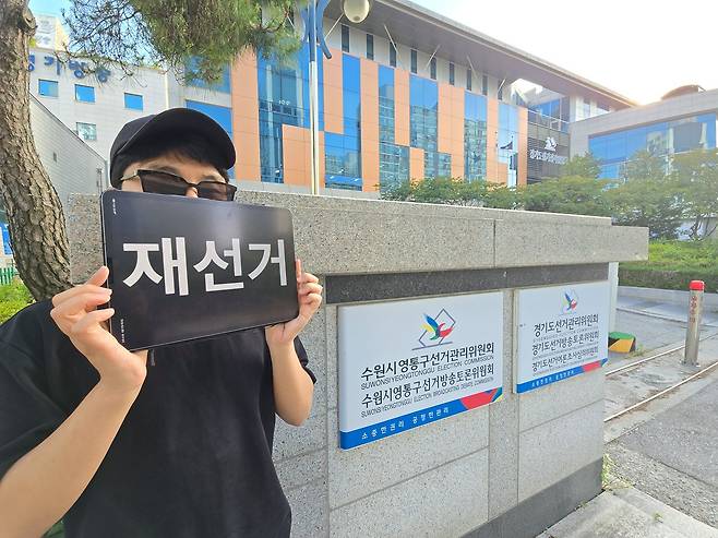 경기도 수원에 거주하는 장모(32)씨가 영통구 경기도선거관리위원회, 수원시영통구선거관리위원회 앞에서 재선거 문구를 띄운 태블릿을 들고 있다. 손성배 기자