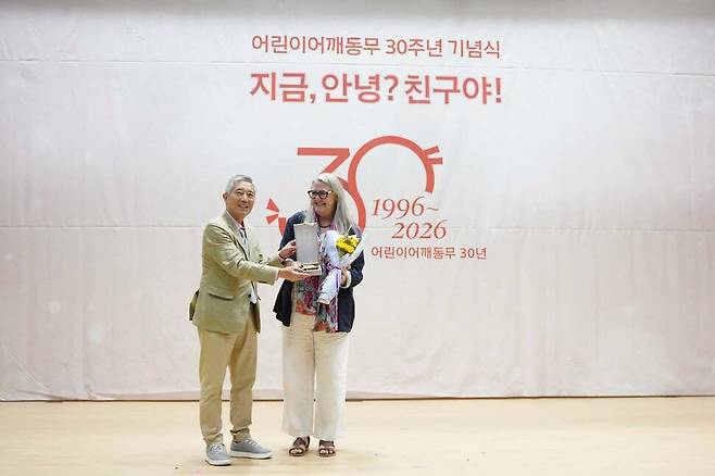 지난 25일 오후 서울 국회 의원회관에서 열린 어린이어깨동무 30주년 기념식에서 이 단체 이기범 이사장(왼쪽)이 지난해 국제 어린이 평화그림전 ‘드로잉 호프’ 가 미국 뉴욕 유엔본부에서 전시될 수 있도록 도움을 준 미쉘 윈트럽 주한 아일랜드 대사에게 어깨동무 평화상을 주고 있다. 어린이어깨동무 페이스북