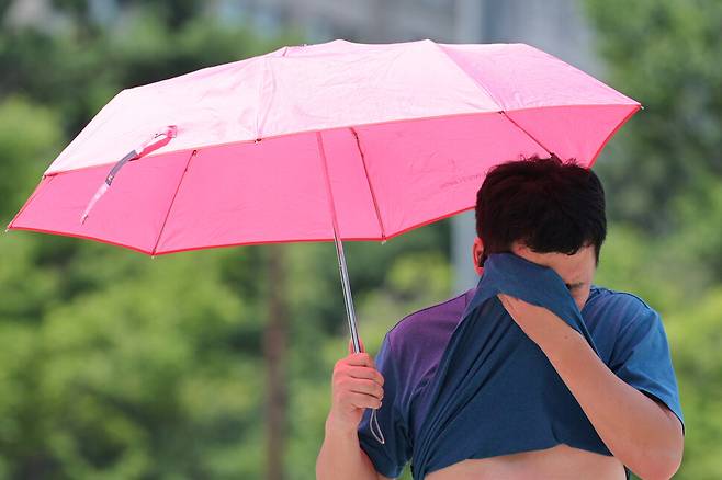 서울 한낮 기온이 35도까지 오르며 무더운 날씨를 보인 12일 서울 영등포구 여의도공원에서 한 시민이 옷으로 땀을 닦아내고 있다. 연합뉴스