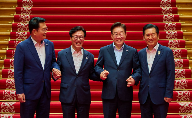 이재명 대통령이 19일 청와대에서 김민석 더불어민주당 대표와 당대표 선거에서 경쟁했던 정청래 전 대표, 송영길 의원 등 참석자들과 손을 맞잡고 기념촬영을 하고 있다. (청와대)