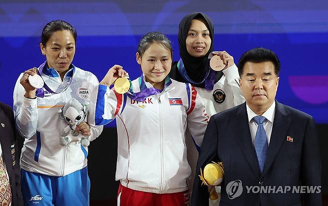 금메달 획득하는 북한 리성금 (나고야=연합뉴스) 김동민 기자 = 23일 일본 나고야 중소기업진흥회관에서 열린 2026 아이치·나고야 아시안게임 역도 여자 49㎏ 결승에서 금메달을 획득한 북한 리성금이 시상대에 올라 김일국 북한 체육상과 기념촬영을 하고 있다.
리성금은 인상 2차 시기 94kg, 용상 2차 시기 121kg를 성공하며 총합 215kg으로 금메달을 획득했다. 2026.9.23 image@yna.co.kr